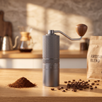 Manual coffee grinder with steel burr on an oak counter with whole coffee beans