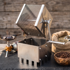 Hand-crank stainless steel drum coffee bean roaster with beans beside a camp stove