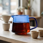 Tinted glass pour-over coffee server with fresh brew on a wooden cafe bar in morning light