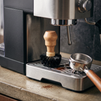 Espresso machine cleaning brush with wood handle on the drip tray below the group head
