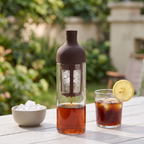 Glass cold drip coffee bottle brewing iced coffee on a summer patio table with a glass of iced coffee