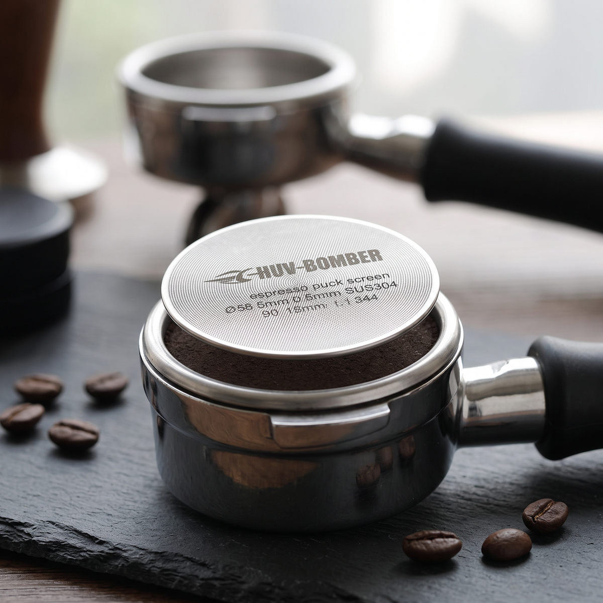 Stainless steel espresso puck screen on a tamped coffee puck in a portafilter on a slate bar